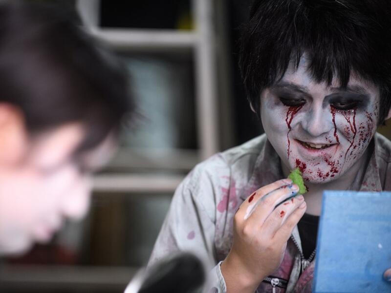 This picture taken on June 15, 2020 shows actor Kenta Iwana (R), 25, putting on zombie makeup before a demonstration of a drive-in haunted house at a garage in Tokyo. A car horn beeps and the horror begins: a bloody murder and rampaging zombies. But this drive-in haunted house in Japan protects against the most terrifying enemy of all -- coronavirus. Inside a car, guests can scream as loudly as they like, with no mask required, as hideous creatures daubed in blood swarm towards them.  Philip FONG / AFP