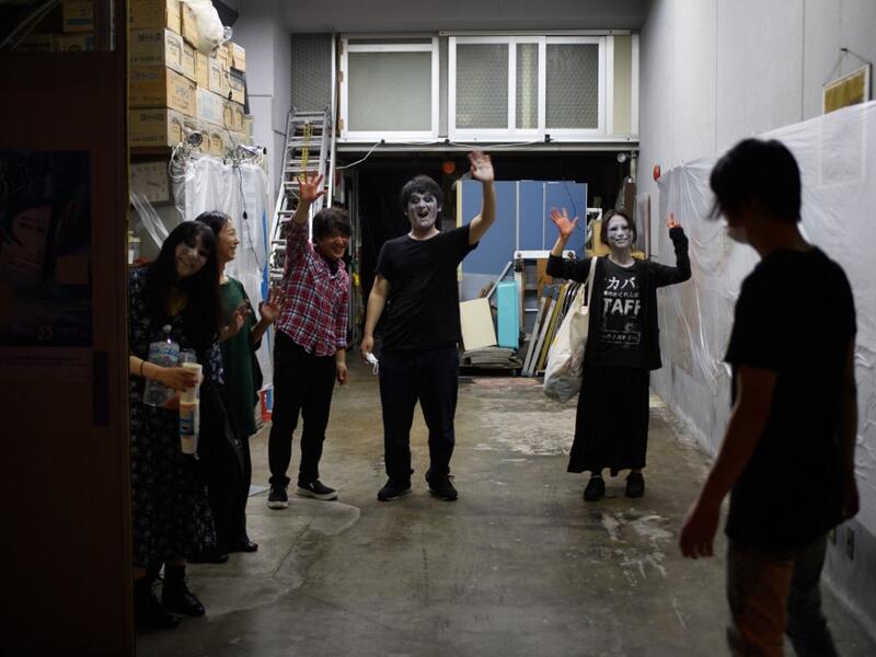 This picture taken on June 15, 2020 shows drive-in haunted house actors (L to R) Haruna Suzuki, 20, Asami Takeuchi, 33, Kota Hanegawa, 28, Kenta Iwana, 25, Ayaka Imaide, 34, and sound and lights engineer Daichi Ono waing to AFP reporters after a demonstration of a drive-in haunted house at a garage in Tokyo. A car horn beeps and the horror begins: a bloody murder and rampaging zombies.Philip FONG / AFP