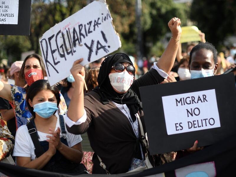 Women hold placrds rading !Legalization now" and "To migrate is not a crime" during a migrant´s demonstration in Barcelona on June 20, 2020, marking World Refugee Day and demanding legal papers for refugees and migrants in Spain. Josep LAGO / AFP