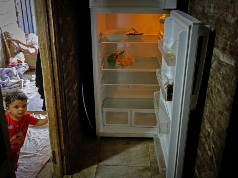 A Lebanese child stands next to an empty refrigerator in their apartment in the port city of Tripoli north of Beirut. Image Credit: AFP