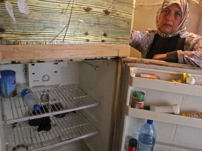 Holding her fridge door open, Fadwa Merhebi explains she already downsized once because she could not afford enough food to fill it up. Now it contains only a bottle of mineral water and two cucumbers. | A Lebanese woman displays the content of her refrigerator. Image Credit: AFP