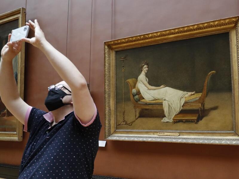 A woman wearing face mask takes a pictures as she visit the Louvre Museum in Paris on July 6, 2020, on the museum' s reopening day. FRANCOIS GUILLOT / AFP