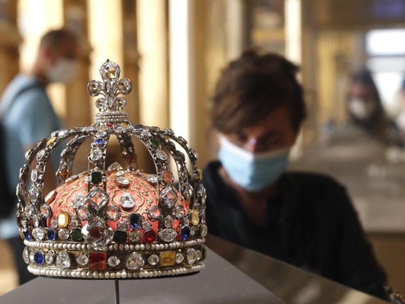 A visitor wearing face mask stands in front of the Crown of Louis XV held in the Apollo gallery at the Louvre Museum in Paris on July 6, 2020, on the museum' s reopening day. FRANCOIS GUILLOT / AFP