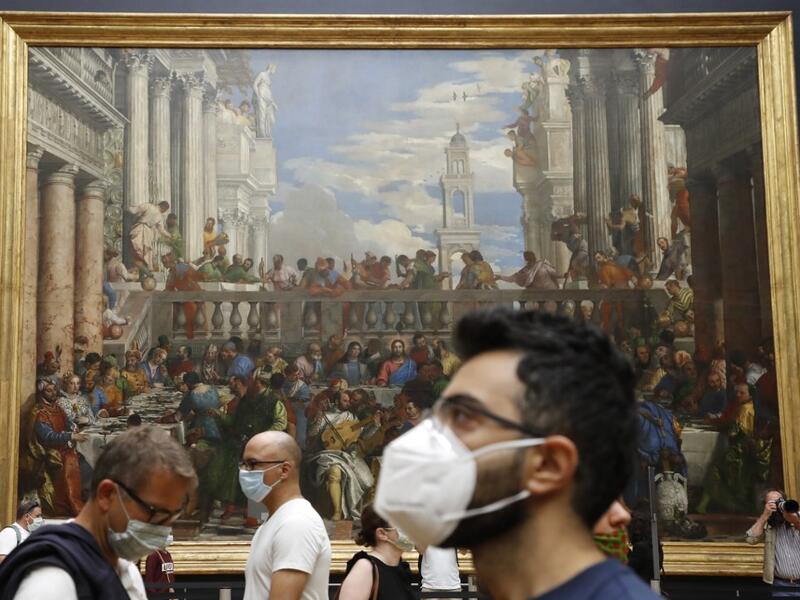 Visitors wearing face mask stands in front of " The Wedding Feast at Cana " oil on canvas painting by the Italian artist Paolo Veronese (1528–1588) at the Louvre Museum in Paris on July 6, 2020, on the museum' s reopening day.FRANCOIS GUILLOT / AFP