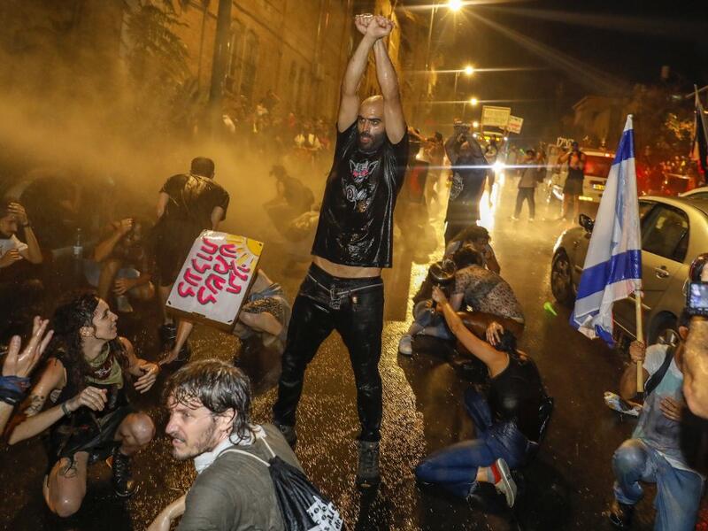 A protester holds up his fists as Israeli police spray the crowd with water cannon during a rally against Prime Minister Benjamin Netanyahu in Jerusalem, on July 19, 2020 amid the coronavirus pandemic. Israeli police fired water cannons to disperse anti-government protests attended by thousands on Saturday, as public anger mounts over the handling of the coronavirus crisis. 