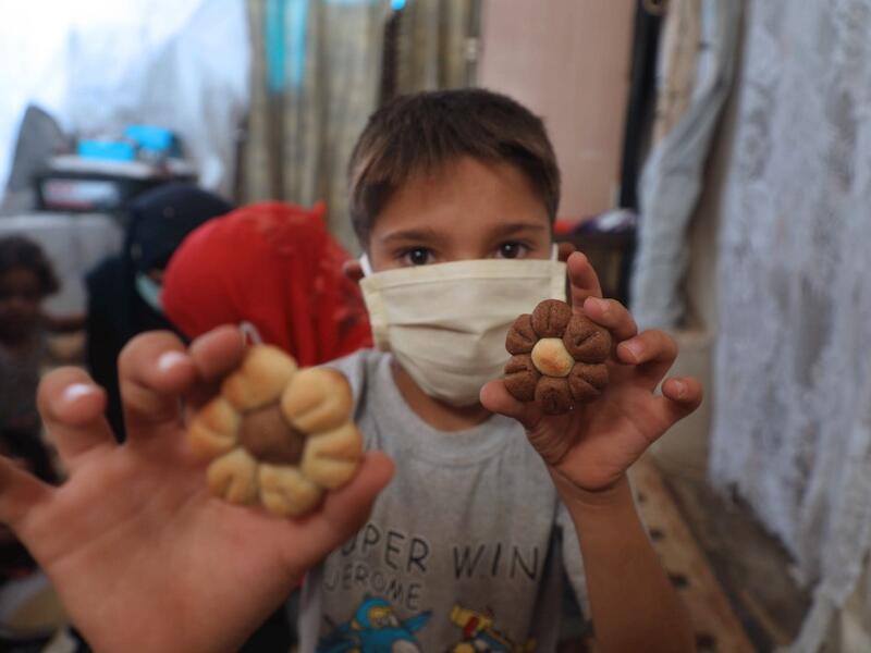 A displaced Syrian boy, wearing protective a face mask, displays cookies to the camera at a camp for the internally displaced near the town of Sarmada in Syria's northwestern Idlib province on July 29, 2020, as Muslims across the world are getting ready to celebrate Eid al-Adha. AAREF WATAD / AFP