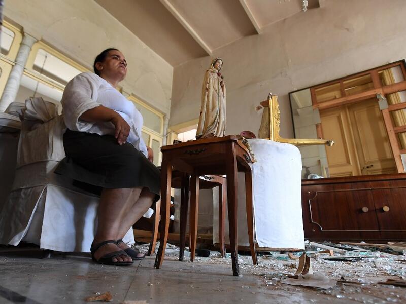 A woman sits next to a statue of Virgin Mary in her damaged house in the Lebanese capital Beirut on August 6, 2020, two days after a massive explosion shook the Lebanese capital. The blast, which appeared to have been caused by a fire igniting 2,750 tonnes of ammonium nitrate left unsecured in a warehouse, was felt as far away as Cyprus, some 150 miles (240 kilometres) to the northwest. The scale of the destruction was such that the Lebanese capital resembled the scene of an earthquake, with thousands of pe