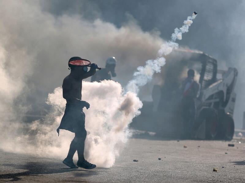 A topless protester wearing a gas mask uses a racket to volley back a tear gas canister during clashes with security forces in downtown Beirut on August 8, 2020, following a demonstration against a political leadership they blame for a monster explosion that killed more than 150 people and disfigured the capital Beirut. PATRICK BAZ / AFP
