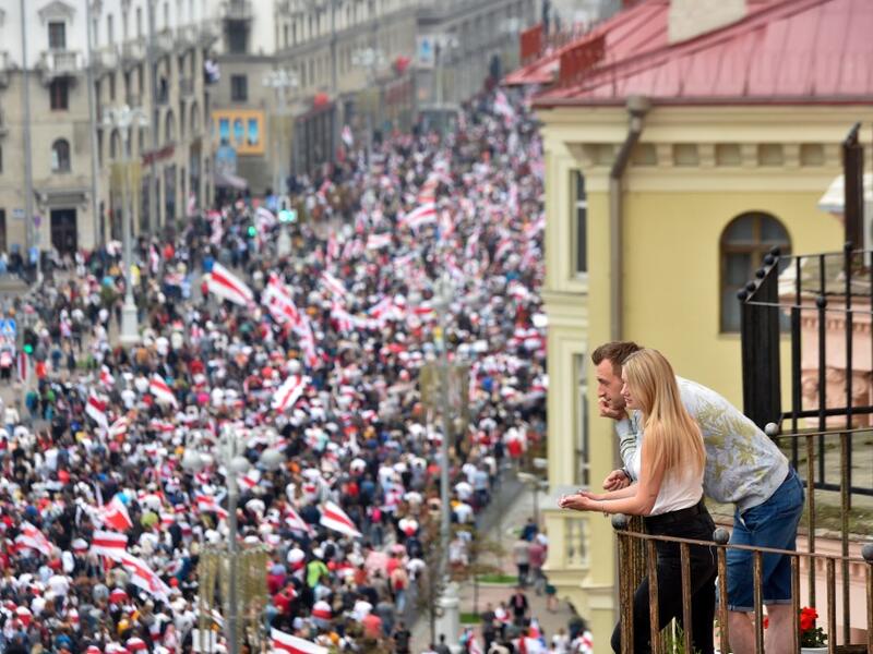 A couple looks at demonstrators from a balcony during a march of opposition supporters to protest against disputed presidential elections results in Minsk on August 23, 2020. Sergei GAPON / AFP