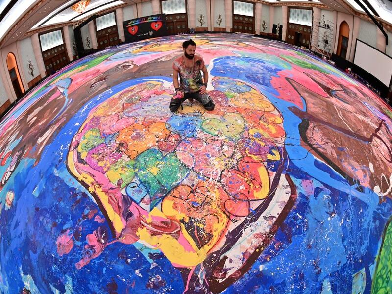 Contemporary British artist Sacha Jafri (C) stands on his record-breaking painting entitled 'The Journey of Humanity' on September 23, 2020, in the Emirati city of Dubai. The painting, which measures the size of two football fields, can be seen at a hotel in Dubai, where Jafri spent months of lockdown due to the coronavirus pandemic. The gigantic artwork is part of his project 'Humanity Inspired' and with it he hopes to raise 30 million USD to fund health and education initiatives for children living in pov