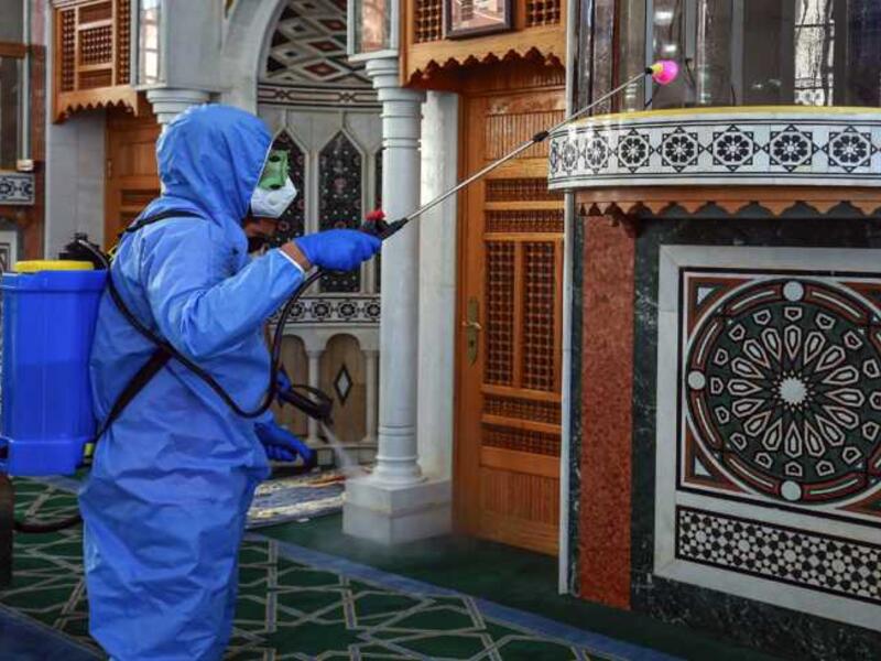 A worker dressed in personal protective equipment sterilizes the mihrab of a mosque in Jordan's capital Amman on June 3, 2020, ahead of its reopening. Photo by KHALIL MAZRAAWI/AFP via Getty Images.