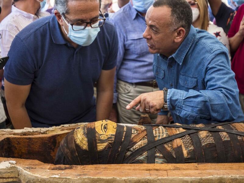 A picture taken on October 3, 2020 shows Egyptian Minister of Tourism and Antiquities Khaled Al-Anani (L), and Mustafa Waziri (R), Secretary General of the Supreme Council of Antiquities, unveil the mummy inside a sarcophagus excavated by the Egyptian archaeological mission working at the Saqqara necropolis, 30 kms south of the capital Cairo, which resulted in the discovery of a deep burial well with more than 59 human coffins closed for more than 2,500 years. They were unearthed south of Cairo in the spraw