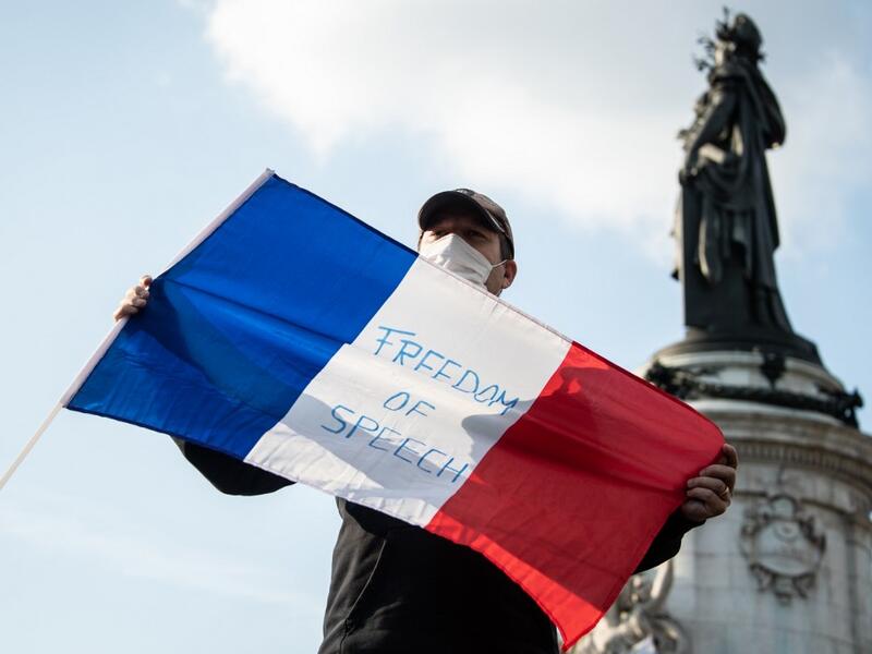 A man holds a French flag as people gather on Place de la Republique in Paris on October 18, 2020, in homage to history teacher Samuel Paty two days after he was beheaded by an attacker who was shot dead by policemen. BERTRAND GUAY / AFP