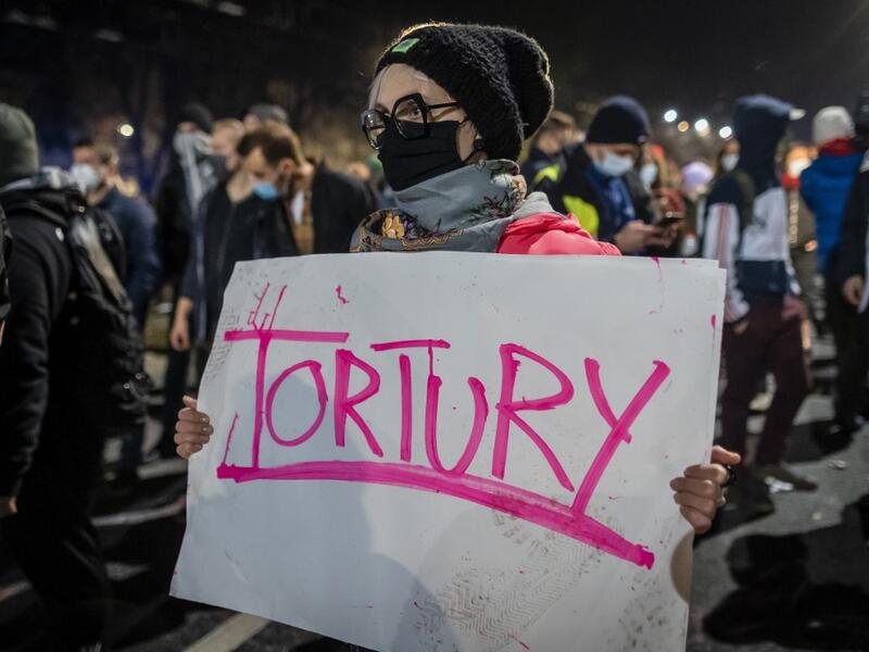 A protestor blocked by riot police guarding the house of Jaroslaw Kaczynski, leader of Poland's ruling Law and Justice party (PIS)holds a poster reading "torture" during a demonstration against a decision by the Constitutional Court on abortion law restriction,in Warsaw on October 23, 2020. Wojtek RADWANSKI / AFP