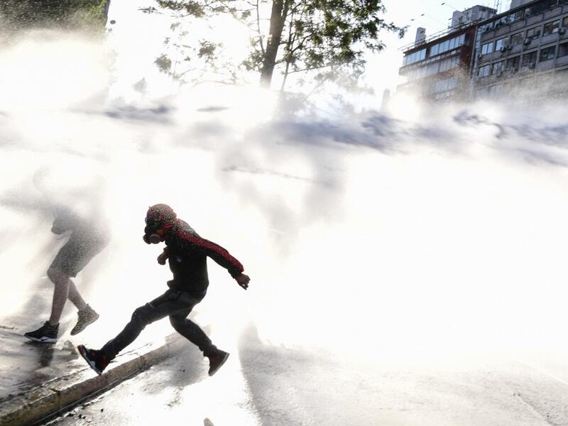 Demonstrators are sprayed with water canons by riot police in a protest against Chilean President Sebastian Pinera's government during the constitutional referendum voting day at Plaza Italia square in Santiago on October 25, 2020. A year to the day after more than one million people thronged downtown Santiago in the biggest Chile's social uprising, Chileans vote Sunday on whether to change the country's dictatorship-era constitution seen as underpinning the nation's glaring inequalities. Martin BERNETTI / 