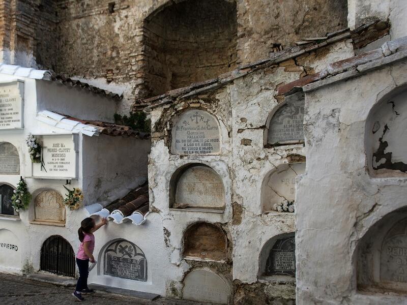 A girl touches a grave at the Cemetery of Villaluenga del Rosario near Cadiz on All Saints' Day on November 1, 2020. The Cemetery of Villaluenga is built on the ruins of the El Salvador Church which was burnt during the war of independence. CRISTINA QUICLER / AFP