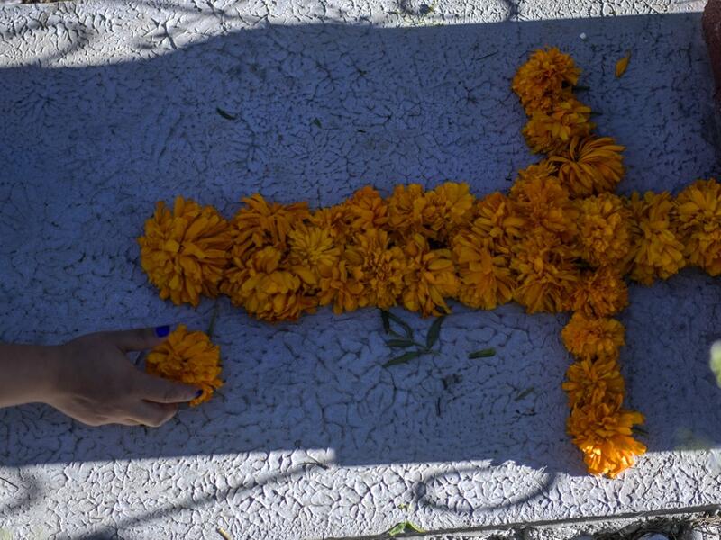 A woman decorates a relative's grave with Mexican marigolds forming a cross at La Magdalena Pantheon, in San Pedro Cholula, Puebla state, Mexico, on November 1, 2020, on All Saints' Day, amid the COVID-19 coronavirus pandemic. Local authorities have restricted the visit times and the number of visitors in cemeteries due to the pandemic. PEDRO PARDO / AFP