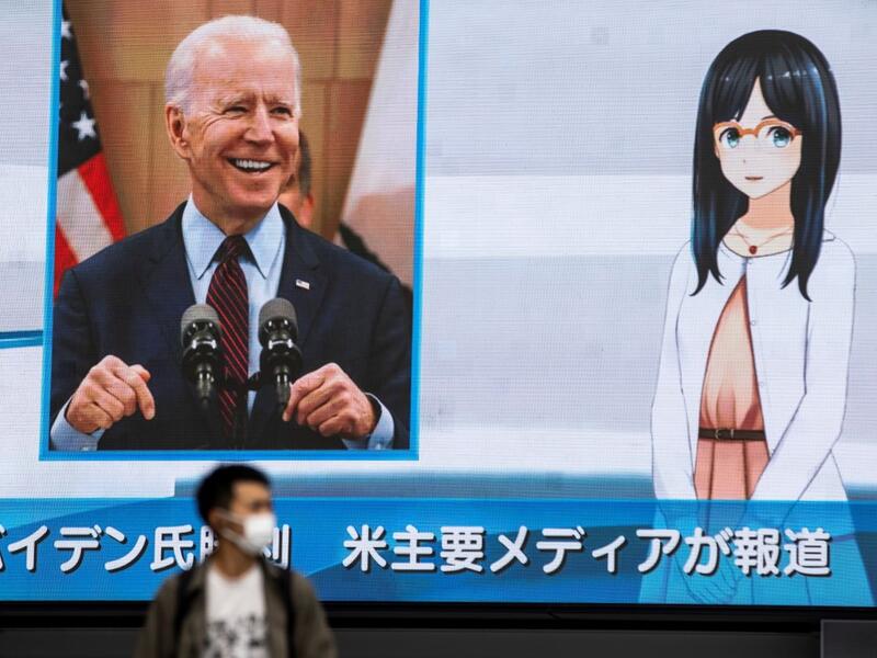 A man wearing a face mask walks in front of a huge screen showing a news programme featuring US Democratic candidate Joe Biden's win in the US presidential election, in Tokyo on November 8, 2020. Behrouz MEHRI / AFP