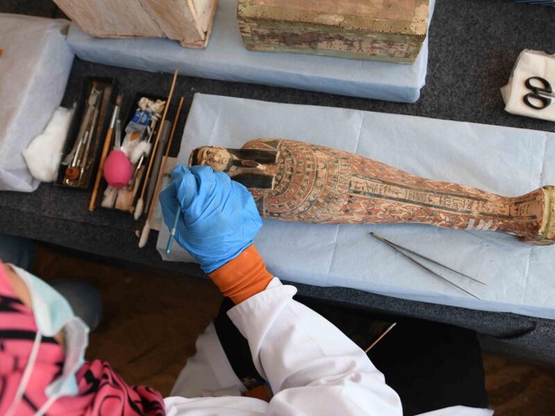 An archaeologist cleans a statue during the unveiling of an ancient treasure trove of more than a 100 intact sarcophagi, at the Saqqara necropolis 30 kms south of the Egyptian capital Cairo, on November 14, 2020. Egypt announced the discovery of an ancient treasure trove of more than a 100 intact sarcophagi, the largest such find this year. The sealed wooden coffins, unveiled on site amid fanfare, belonged to top officials of the Late Period and the Ptolemaic period of ancient Egypt. They were found in thre