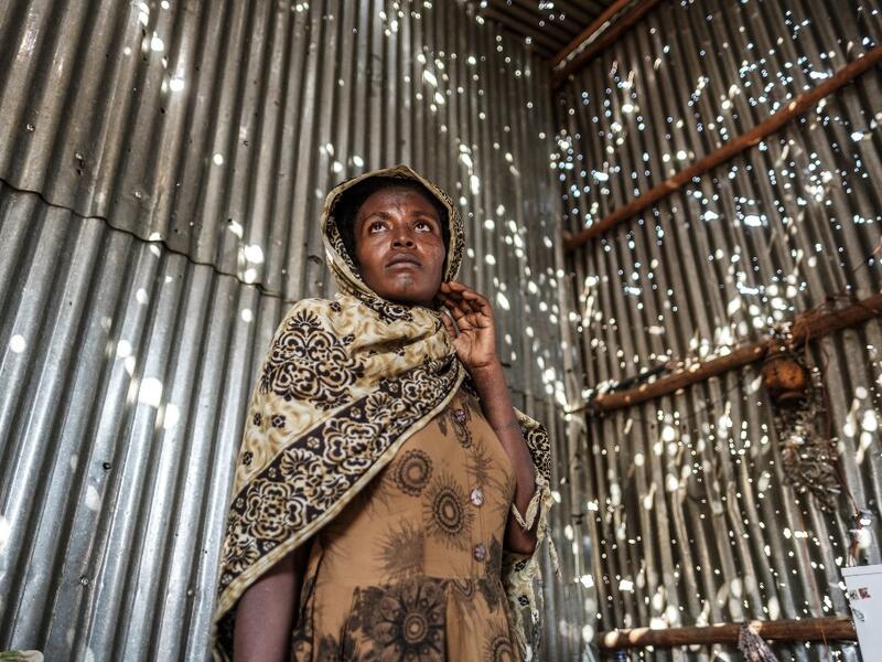 A woman stands in a metal sheet room that was damaged by shelling, in Humera, Ethiopia, on November 22, 2020. In that residential compound, two women and an elderly man were killed by shelling and gunfire, while two other women remain on makeshift stretchers as they recover from their wounds. EDUARDO SOTERAS / AFP