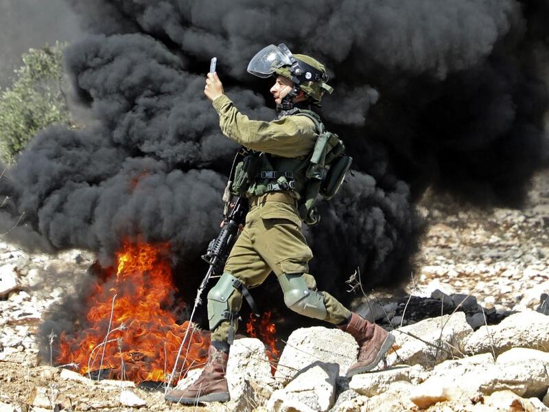 A member of the Israeli security forces takes a photograph with his telephone during clashes with Palestinian protesters after a weekly demonstration in the West Bank village of Kfar Qaddum, on October 23, 2020. JAAFAR ASHTIYEH / AFP