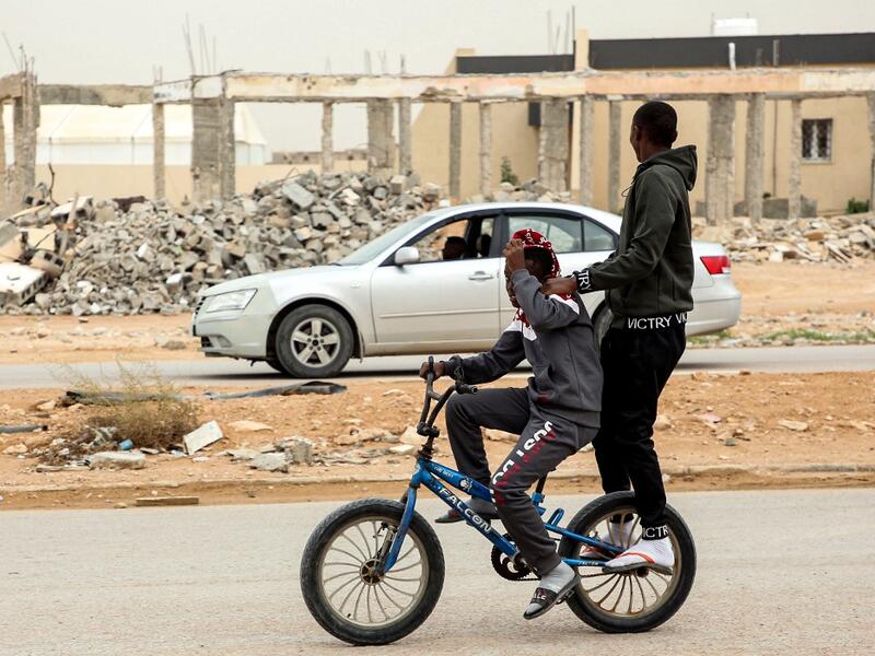 A boy rides behind another on a bicycle along a road past destroyed buildings in the city of Tawergha, some 200 kilometres (125 miles) east of Libya's capital close to the port city of Misrata, on December 12, 2020. When Libyan dictator Moamer Kadhafi was toppled, people took revenge on those they saw as his supporters -- including the entire town of Tawergha, whose 40,000 residents were forced to flee. Now, almost a decade later since militia forces rampaged through the town torching homes, destroying buil