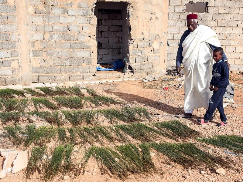Mahmud Abu al-Habel, a 70-year-old resident of Tawergha who was among the first who returned to the city after fleeing in the aftermath of the toppling of Kadhafi, stands outside a damaged house with a boy in the city of Tawergha, some 200 kilometres (125 miles) east of Libya's capital close to the port city of Misrata, on December 12, 2020. When Libyan dictator Moamer Kadhafi was toppled, people took revenge on those they saw as his supporters -- including the entire town of Tawergha, whose 40,000 resident