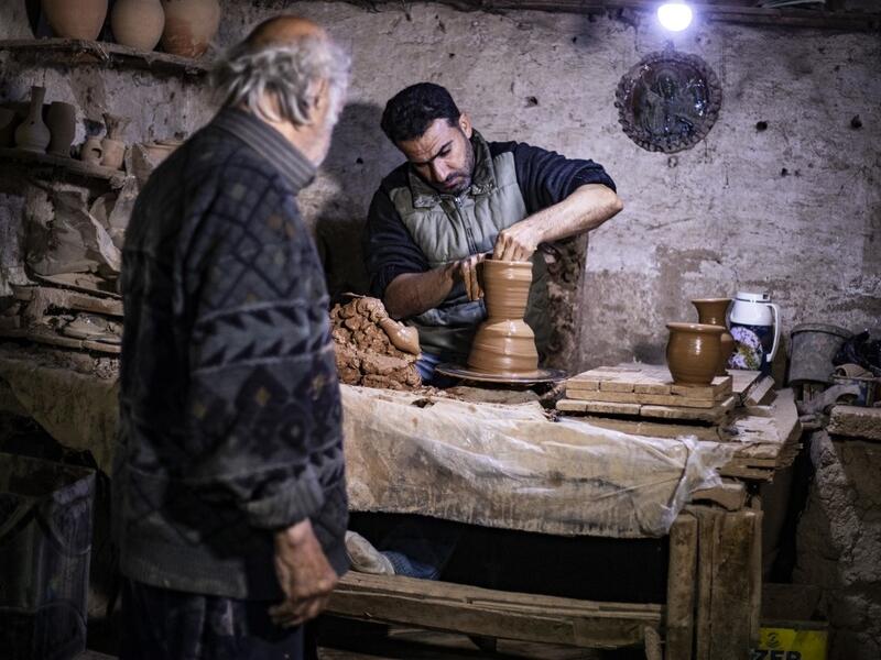 Syrian-Armenian potter Misak Antranik Petros watches his son Anto moulding a clay vase at his workshop located inside an ancient mud-brick house near the city of Qamishli in Syria's northeastern Hasakeh province, on December 19, 2020. Petros was only a teenager when he had to take over for his sick father and become the main potter of the family. He has since become a master of the craft, and is keen to pass his skills on.  Delil SOULEIMAN / AFP