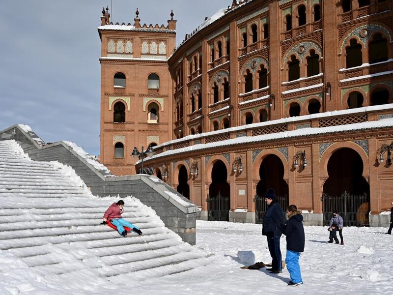A woman slides down steps outside the Las Ventas bullring in Madrid on January 10, 2021. Snowstorms in Spain left three people dead and caused chaos across much of the country, trapping motorists and shutting down the capital's air and rail links. Gabriel BOUYS / AFP