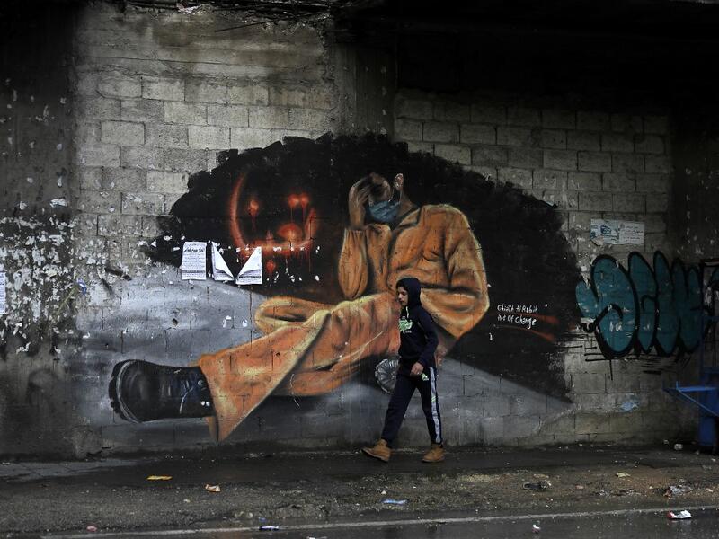 A young boy walks past a mural painting with writing in Arabic that reads "we are tired" near Al-Nour square in the northern city of Tripoli, following overnight clashes between security forces and anti-government protesters, on January 29, 2021. More than 400 people have been wounded in northern Lebanon this week in clashes between security forces and protesters angered by a coronavirus lockdown they say is starving them. JOSEPH EID / AFP