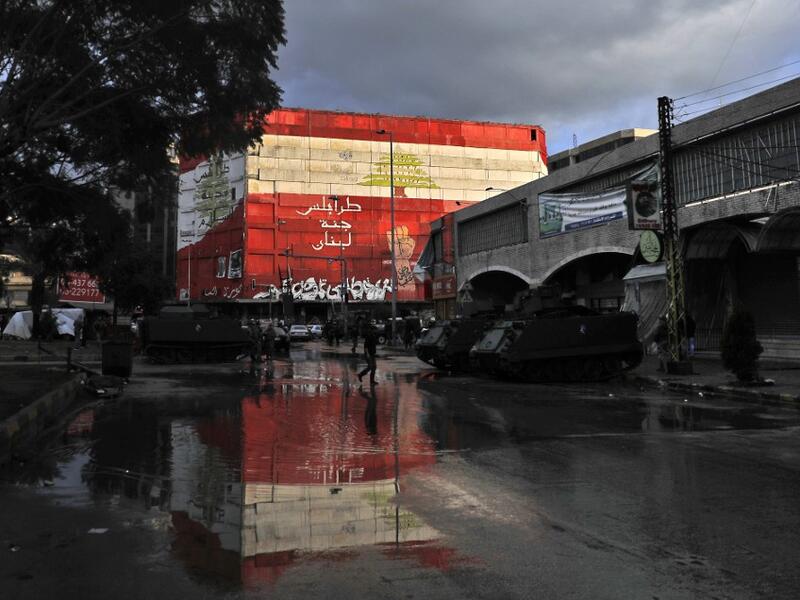 A picture taken on January 29, 2021 shows armoured personnel carriers parked under a mural in Al-Nour square in the Lebanese northern city of Tripoli, following overnight clashes between security forces and anti-government protests. More than 400 people have been wounded in northern Lebanon this week in clashes between security forces and protesters angered by a coronavirus lockdown they say is starving them. JOSEPH EID / AFP
