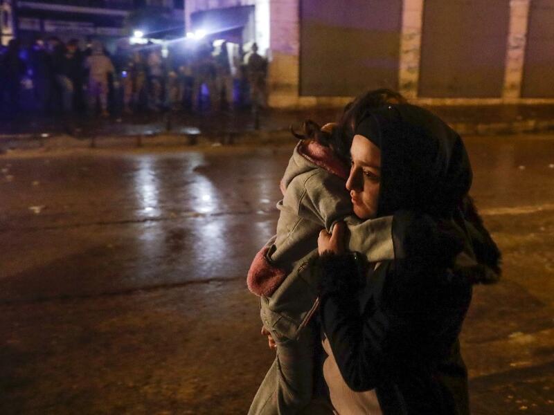 A woman crosses a street with her child during clashes between security forces and anti-government protesters in the northern city of Tripoli, on January 29, 2021. More than 400 people have been wounded in northern Lebanon this week in clashes between security forces and protesters angered by a coronavirus lockdown they say is starving them. JOSEPH EID / AFP