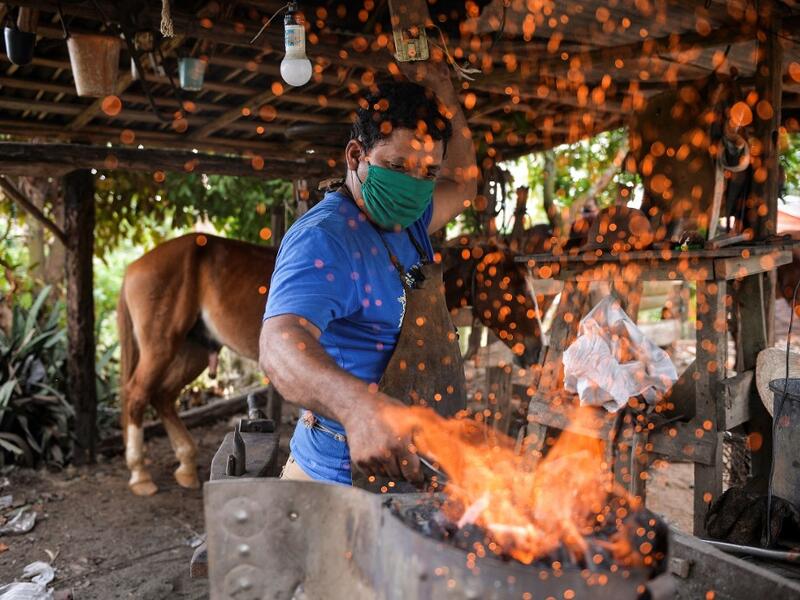 Yusmani Garcia, a blacksmith and tour guide, makes a horseshoe at his house in Vinales, Cuba, on January 28, 2021. At the foot of the majestic rock formations of Vinales, the terraces of the restaurants look empty and the lodgings have closed. With the arrival of COVID-19, the incipient prosperity of this Cuban town came to a halt and people abandoned tourism jobs to return to work the land. YAMIL LAGE / AFP