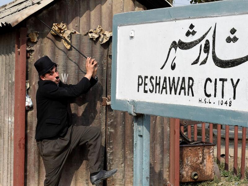 In this picture taken on February 9, 2021, street actor Usman Khan, dressed up as silent film star Charlie Chaplin, performs in the Pakistan's northwestern city of Peshawar. Wearing a bowler hat and familiar toothbrush moustache, Pakistan's Usman Khan darts through traffic swinging a cane, teasing motorists and shopkeepers for laughs and a few rupees with a Charlie Chaplin impersonation that has become a viral sensation.  Abdul MAJEED / AFP