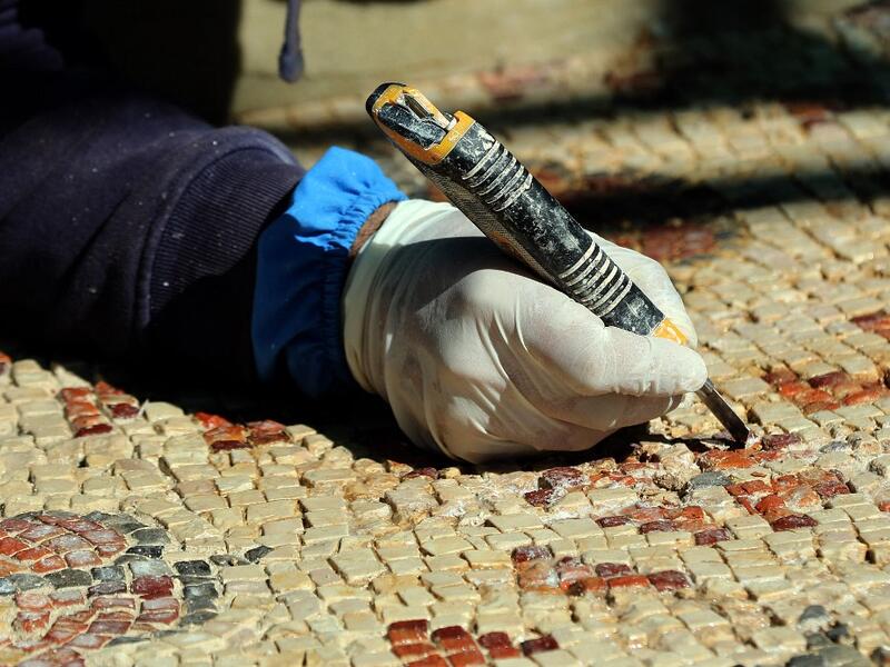 A worker employed by a pilot project run by the UN cultural agency UNESCO, restores a mosaic floor at an ancient church complex, in the small town of Rihab, some 70 kilometres north of the Jordanian capital Amman, on February 9, 2021. In the ruins of the ancient Byzantine church in Jordan, local townspeople and Syrian refugees work side by side on a project that unites preserving cultural heritage and fighting poverty.  Khalil MAZRAAWI / afp
