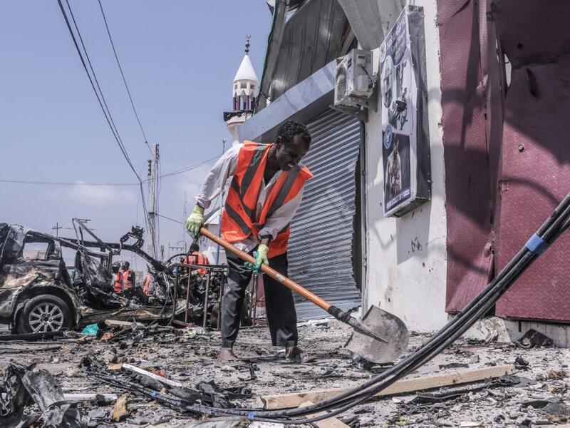 A rescue worker clears debris with a shovel at the site of a suicide car bombing attack near a security checkpoint in Mogadishu on February 13, 2021. Three people were killed and eight wounded after a car bomb detonated near a security checkpoint in the Somali capital Mogadishu, a security official and witnesses said. Abdirazak Hussein FARAH / AFP