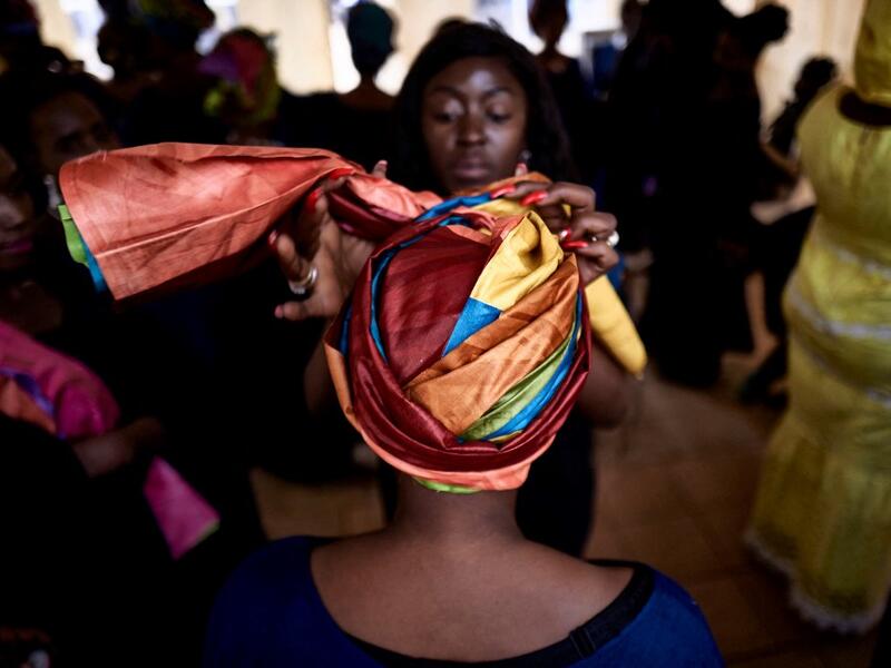 A dresser helps a gold miner to wear a turban in the backstage prior to take part in a fashion show as part of the first edition of the International Gold Fair Afrik'Or, in Bamako, on February 12, 2021. The Princess of Burundi Esther Kamatari, selected 34 women among gold mines workers in southern Mali, to walk down the catwalk for a fashion show organised during the International Gold Fair. Gold represents 15% of Mali's exports and more than 20% of its GDP estimated at nearly US$20 billion by the end of 20