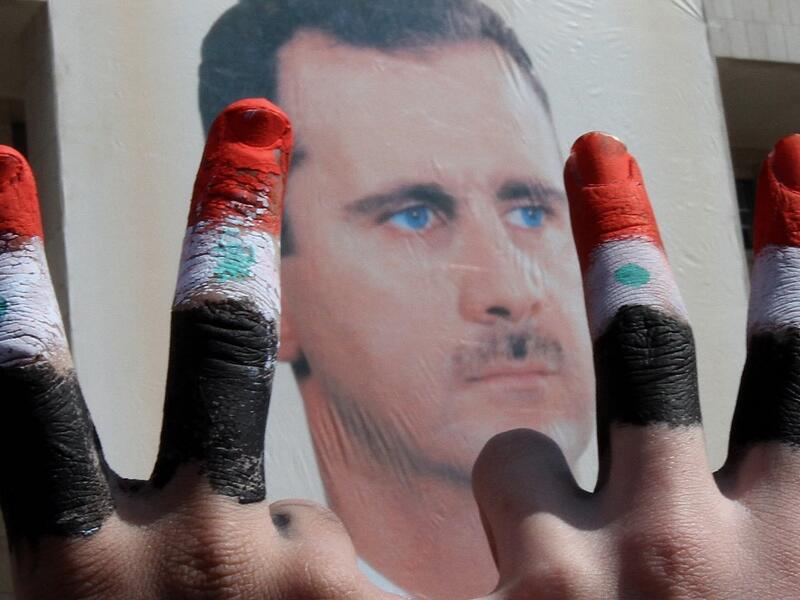  Two men, with the fingers painted in the colours of the Syrian flag, show the V-sign as they pose in front of a huge image of President Bashar al-Assad 