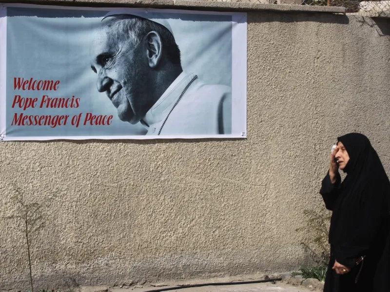 An Iraqi woman walks in front of a banner welcoming Pope Francis