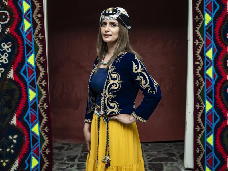A Syrian Kurdish woman in traditional attire poses for a picture 
