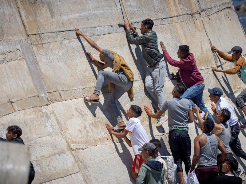 Migants climb a sea wall in the northern town of Fnideq after attempting to cross the border from Morocco to Spain's North African enclave of Ceuta on May 19, 2021. Spain stepped up diplomatic pressure on Rabat as its prime minister flew into Ceuta, vowing to "restore order" in the North African enclave after a record 8,000 migrants reached its beaches from Morocco