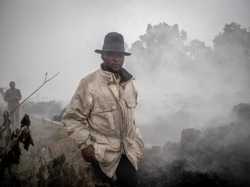 Men cross the front of the still smoking lava rocks from an eruption of the Mount Nyiragongo on May 23, 2021 in Goma in the East of the Democratic Republic of Congo. A river of boiling lava came to a halt on the outskirts of Goma Sunday, sparing the city in eastern DR Congo 