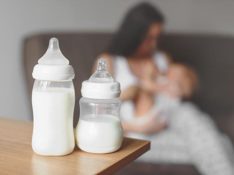 Bottles with breast milk on the background of mother holding in her hands and breastfeeding baby