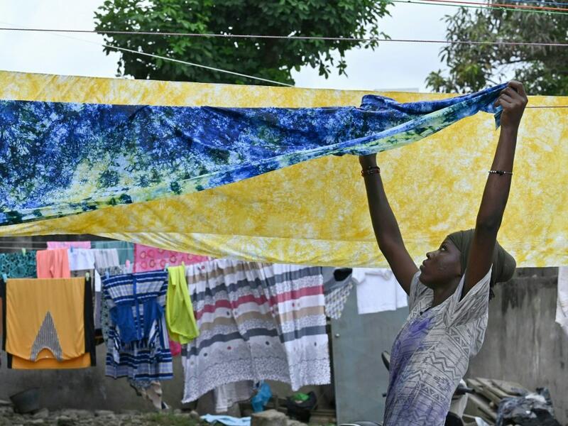 A woman hangs up dyed cotton fabric to dry at Pathe'O house in the popular district of Treichville in Abidjan on March 31, 2021. A small self-taught tailor in his early years, the Ivorian-Burkinabe Pathe'O became the designer of African heads of state and celebrates the fiftieth anniversary of his brand, leading the "fight" for the recognition of fashion on the continent