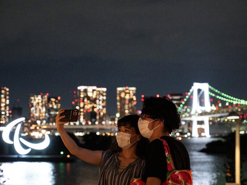 This picture taken on August 21, 2021 shows people taking pictures before the Paralympic Games symbol lit up at night on the Odaiba waterfront in Tokyo. 