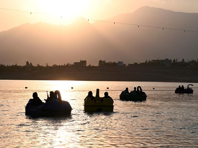 In this photograph taken on September 28, 2021 Taliban fighters ride on paddle boats at Qargha Lake on the outskirts of Kabul. "This is Afghanistan!" a Taliban fighter shouts on the pirate ship ride at a fairground in western Kabul, as his armed comrades cackle and whoop on board the rickety attraction. (Photo by WAKIL KOHSAR / AFP) / TO GO WITH: AFGHANISTAN-CONFLICT-FAIRGROUND, SCENE BY JAMES EDGAR - TO GO WITH: Afghanistan-conflict-fairground, SCENE by James EDGAR