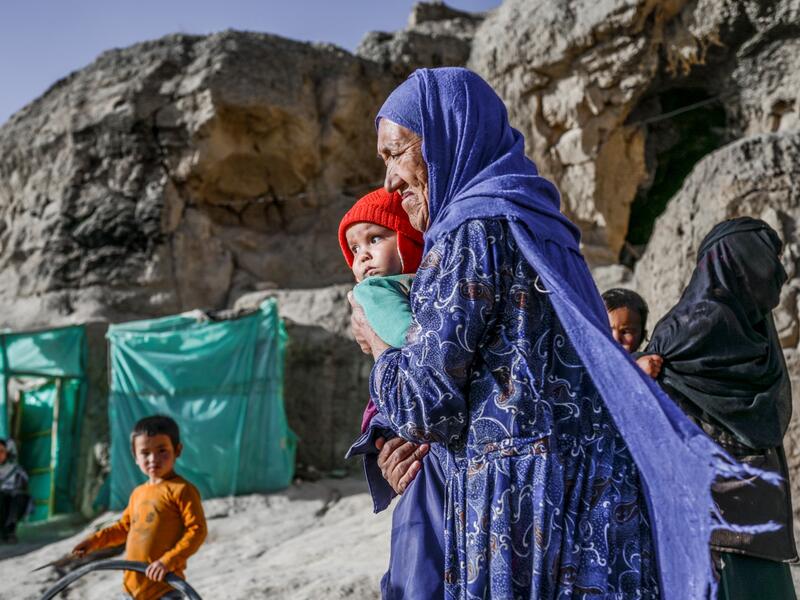 In this picture taken on October 3, 2021, a Hazara ethnic woman with a baby walks in front of her cave on a cliff pockmarked by caves where people still live as they did centuries ago in Bamiyan. 