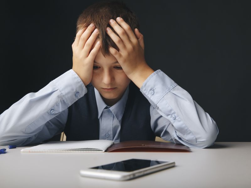 Cyberbullying concept. Stressed and upset school boy with gadget isolated.