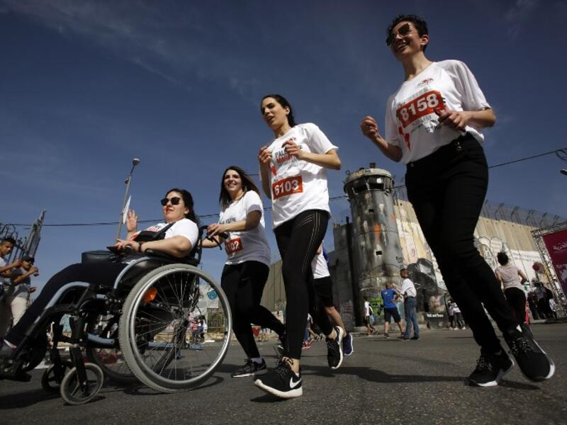 Participants push another in a wheelchair as they run along Israel's controversial separation barrier, which divides the West Bank from Jerusalem, in the biblical town of Bethlehem during the 6th International Palestine Marathon on Mar. 23, 2018. 
(Musa AL SHAER / AFP)