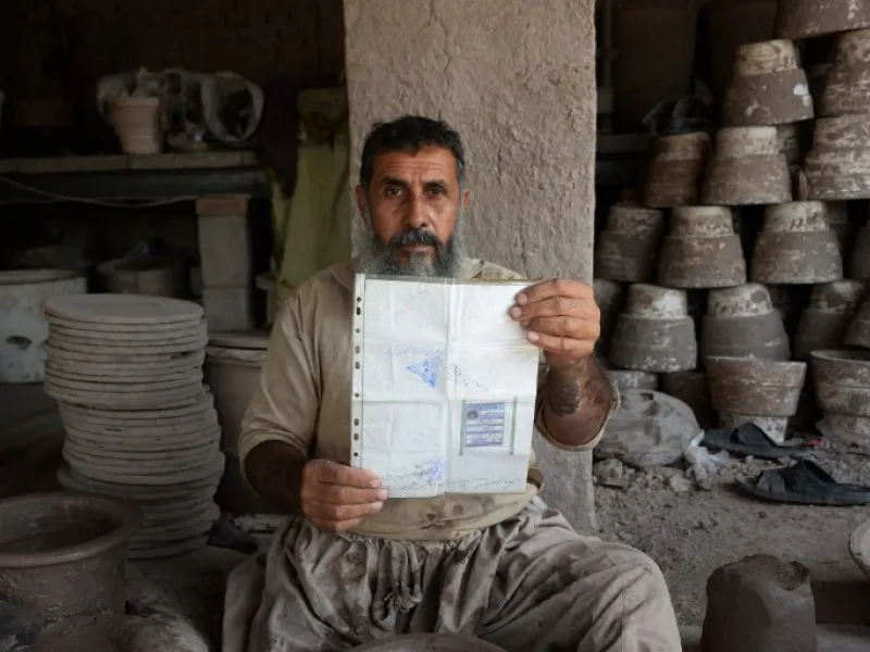 In this photo taken on October 10, 2018.Afghan potter Shirin Agha, 45, poses for a picture as he holds his id card or Tazkira registered to vote in the upcoming parliamentary election at his workshop, on the outskirts of Jalalabad. 
NOORULLAH SHIRZADA / AFP